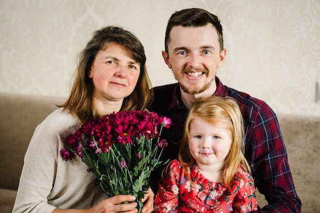 Portret kleindochter vader zoon knuffelen grootmoeder met bloemen thuis glimlachend tijd samen doorbrengen Internationale Vrouwendag Happy Mother's Day Vakantieconcept Familie van drie generaties