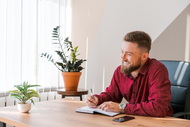 Portret knappe lachende man met baard aan het werk op kantoor aan een project he