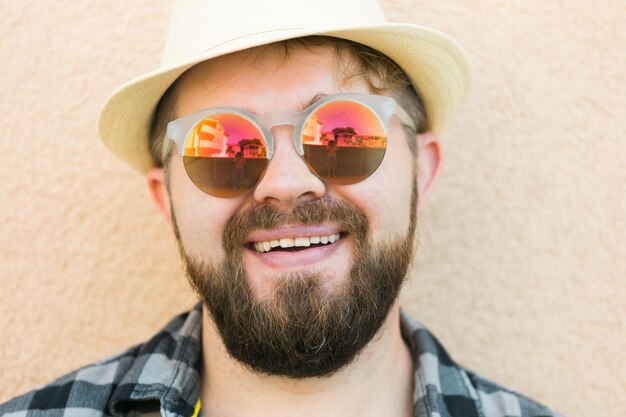 Portret knappe man met zomerhoed en zonnebril en geruit hemd glimlachend gelukkig in de buurt van muurtrav