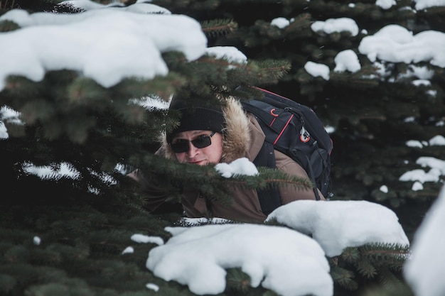 Portret lachende brute jonge man in de open lucht tussen besneeuwde kerstbomen in het winterseizoen in het bos