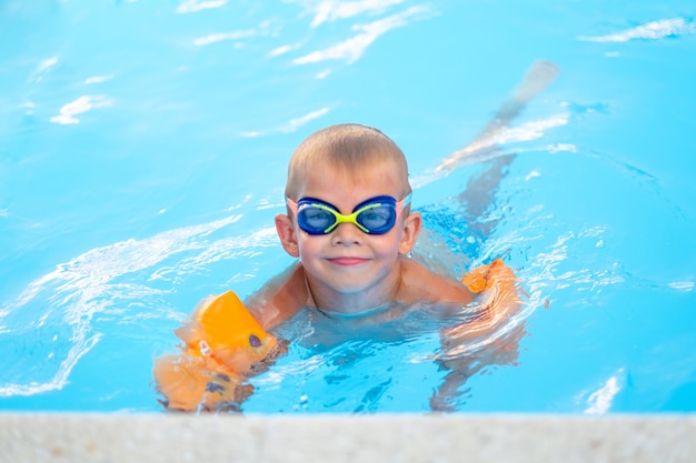 Portret lachende jongen in zwembad kind in zwembril en opblaasbare mouwen zomer reizen