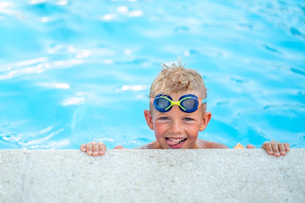 Portret lachende jongen in zwembad kind in zwembril en opblaasbare mouwen zomerreis hotelvakantie of lessen