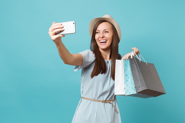 Portret lachende vrouw in zomerjurk, stro hoed met pakketten tassen met aankopen na het winkelen doen selfie schot op mobiele telefoon geïsoleerd op blauwe pastel achtergrond. Ruimte voor advertentie kopiëren