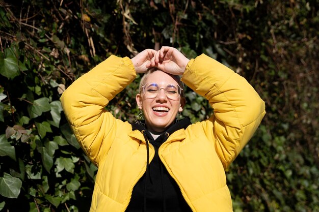 Foto portret lgbti meisje lachend blij met handen op hoofd gele jas natuur en planten