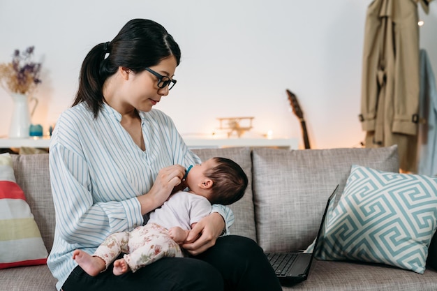 portret liefhebbende aziatische carrièremoeder die thuis werkt, troost haar pasgeboren baby om te slapen terwijl ze haar hand op de fopspeen in de woonkamer houdt.