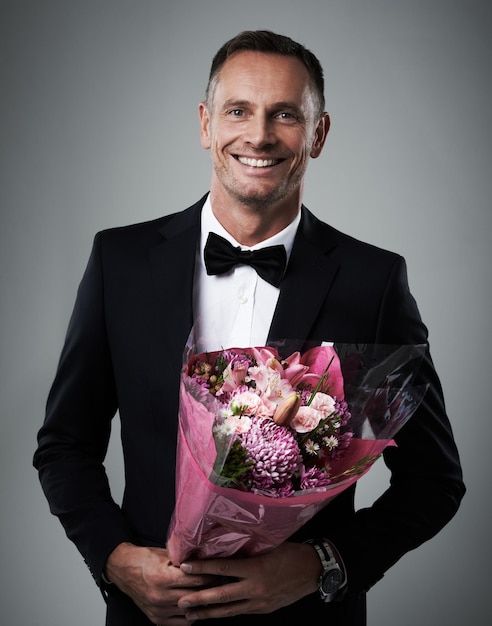 Portret man en boeket bloemen pak en geluk voor Valentijnsdag romantiek en op grijze studio achtergrond Gezicht man en man met bloemen cadeau glimlach en gebaar voor liefde romantisch en gelukkig