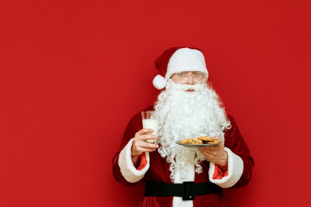 Portret man verkleed als kerstman met glas melk en plaat met chocoladekoekjes