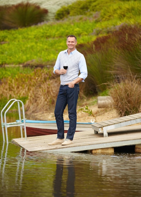 Portret meer en volwassen man met rode wijn vakantie en glimlach op een weekendje weg uitje en geluk Gezicht mannelijke persoon en gelukkige kerel op een zomervakantie alcohol en buiten om te ontspannen en te chillen