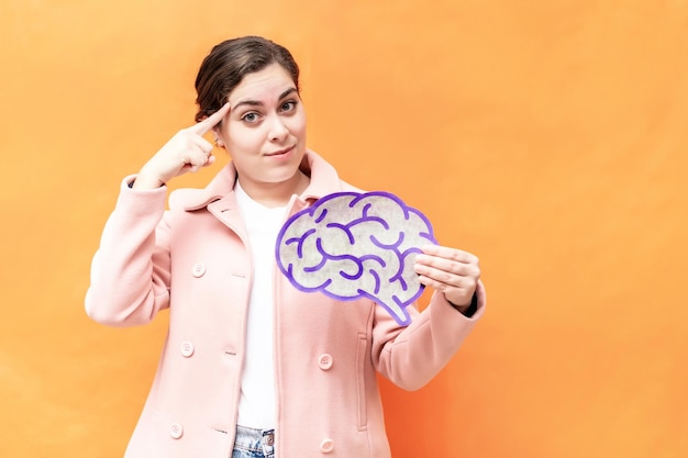 Portret met hersenfiguur en brainstormconcept Zakenvrouw die hersenfiguur op oranje achtergrond houdt Bescherming en zorg voor de geestelijke gezondheid