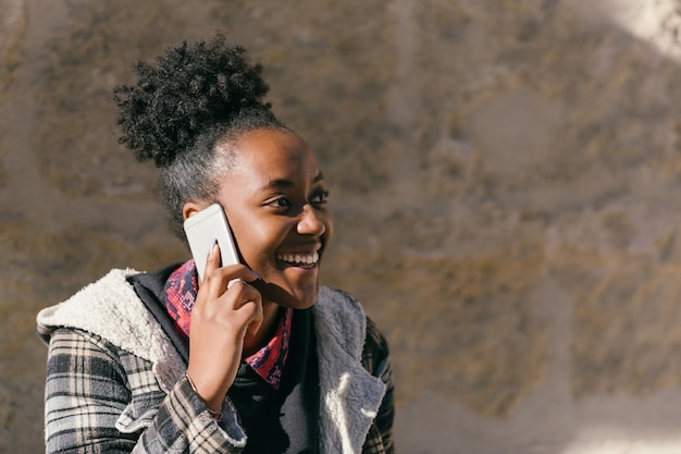 Portret met kopieerruimte van een jonge Afrikaanse vrouw die met de mobiel praat terwijl ze buitenshuis lacht