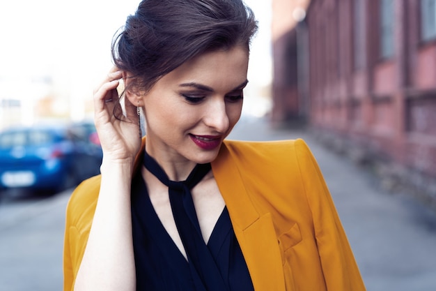Foto portret mode vrouw lopen op straat. ze draagt een gele jas en glimlacht naar de zijkant.