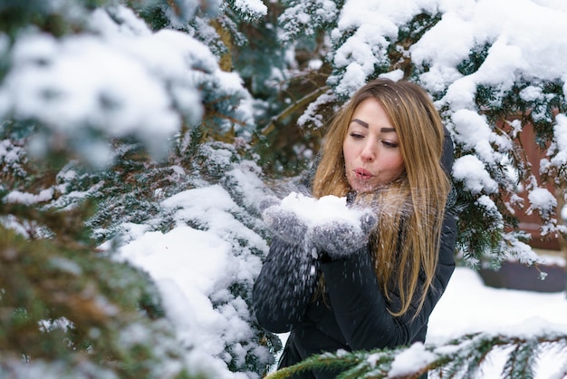 Portret mooi meisje in besneeuwde winterdag in de buurt van dennenboom in bos jonge lachende vrouw spelen met...