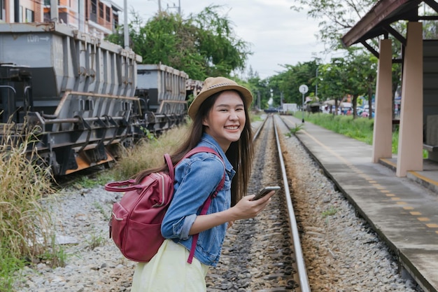 Foto portret mooie aziatische vrouw die met rugzak loopt en geniet van vitalit het treinstation van de rails.