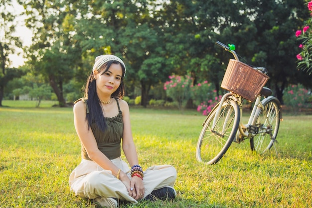 Portret mooie Aziatische vrouw in vrijetijdskleding zittend en lezend een boek op een grasveld naast een witte fiets in een openbaar park