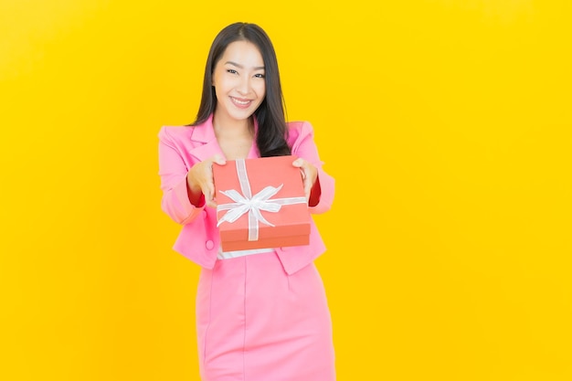 Portret mooie jonge aziatische vrouw glimlach met rode geschenkdoos op gele kleur muur color