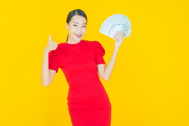 Portret mooie jonge aziatische vrouw glimlach met veel contant geld en geld op geel