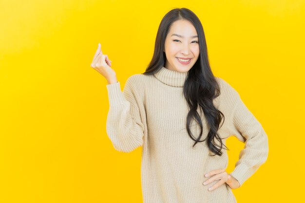 Portret mooie jonge Aziatische vrouw glimlacht met actie op gele muur yellow