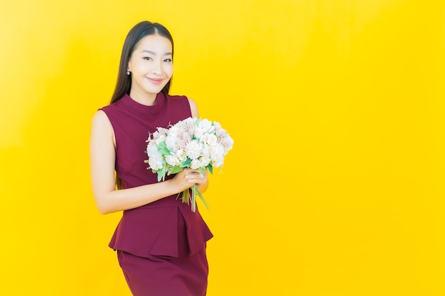 Portret mooie jonge Aziatische vrouw glimlacht met bloem op gele muur