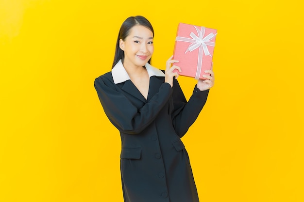 Portret mooie jonge aziatische vrouw glimlacht met rode geschenkdoos op kleurenmuur