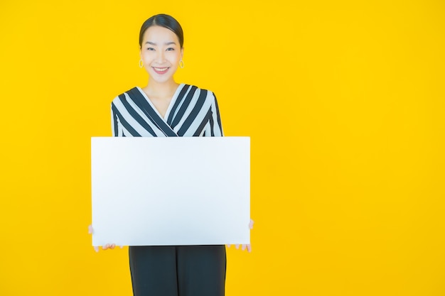 Portret mooie jonge Aziatische vrouw met leeg wit reclamebord op geel