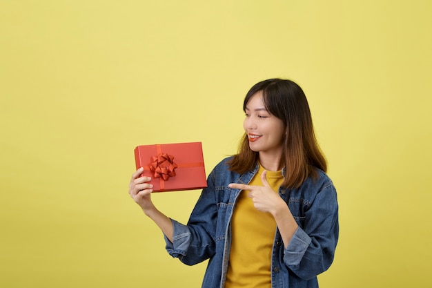 Portret mooie jonge Aziatische vrouw met rode giftdoos op geïsoleerd geel