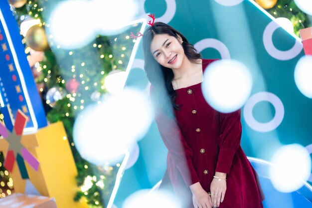 Portret mooie jonge aziatische vrouw rode jurk kostuum en kerstgroet foto perceel decoratie op kerstboom licht circulaire bokeh achtergrond decoratie tijdens kerstmis en nieuwjaar.
