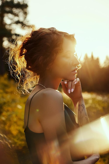 Portret mooie vrouw in bos bij zonsondergang. Vrouw rust in de natuur, een kunstportret in de stralen van de zon