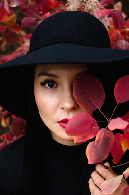 Portret mooie vrouw in een zwarte hoed herfst in rode bladeren