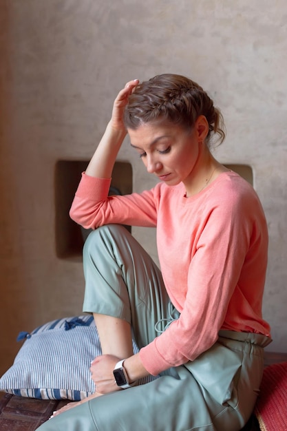 Portret mooie vrouw in koraal sweatshirt en grijze broek zit in de kamer