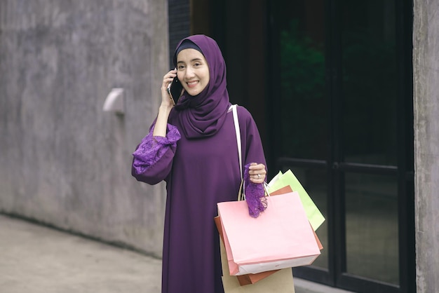 Foto portret moslimvrouw die hijab draagt lopend pratend aan de telefoon en winkelend