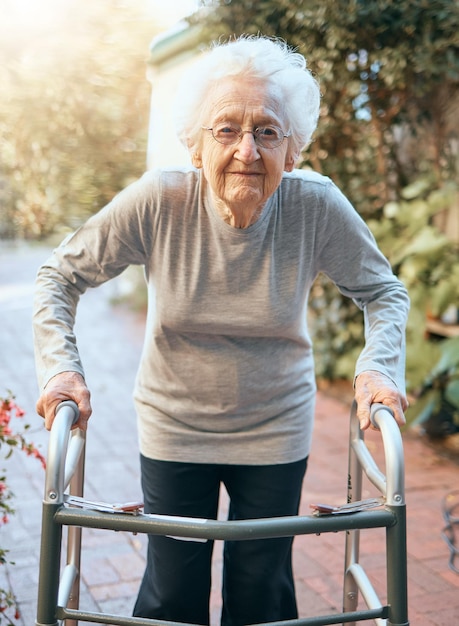 Portret oude vrouw en looprek in park voor gezondheidszorg, wellness en gezonde zonneschijn Vrijheid pensionering en oudere vrouw met handicap buiten in de natuur of tuin alleen voor frisse lucht