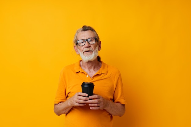 Portret oudere man met zwarte wegwerpbeker gele achtergrond