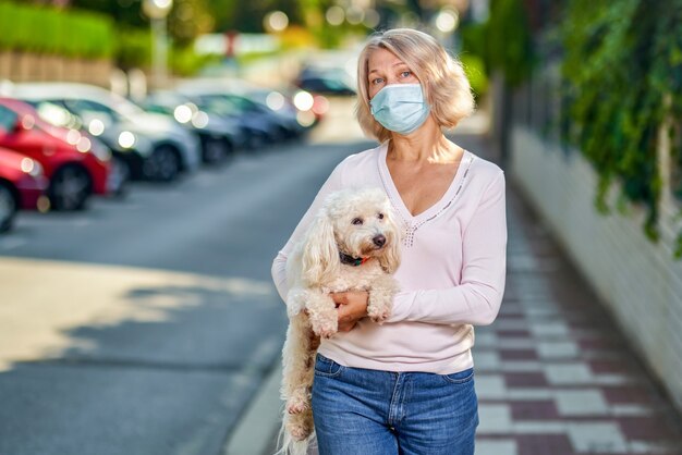 Portret oudere vrouw met een hond buiten een antivirusmasker