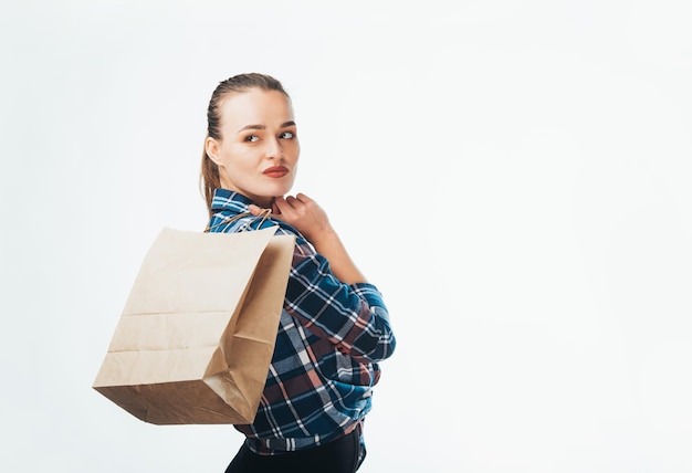 Portret peinzende mooie vrouw met pakket met aankopen na het winkelen geïsoleerd op witte achtergrond Aantrekkelijke jonge nadenkende model met een boodschappentas