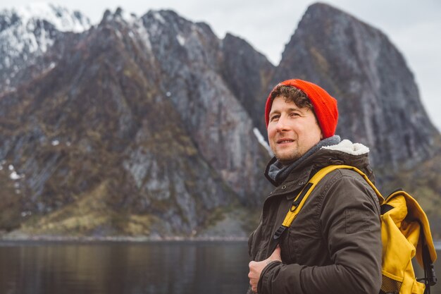 Portret reiziger man met een rode hoed aan de kust op de achtergrond van berg en meer