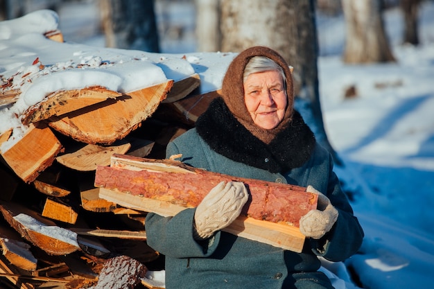 Portret Russische grootmoeder, in het dorp in de winter, brandhout voorbereiden, in Siberië.