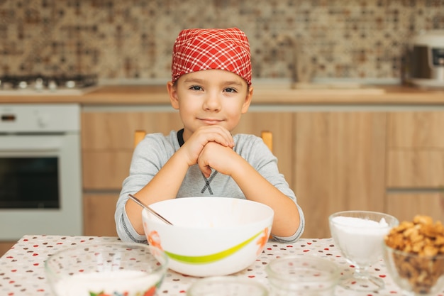 Portret schattige jongen shef op zoek naar camera tijdens het koken