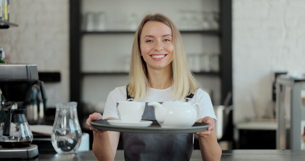 Portret shot van de jonge mooie vrouw barmannen met kopjes koffie op de achtergrond van een koffiezetapparaat. Service, bedrijfsconcept.