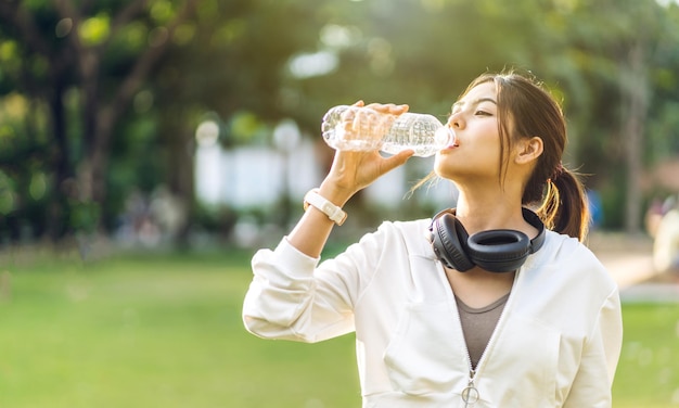 Portret sport Aziatische schoonheid lichaam slanke vrouw drinkwater uit een fles terwijl u ontspant en zich fris voelt op groene natuurlijke achtergrond in zomer groen park Gezonde levensstijl concept