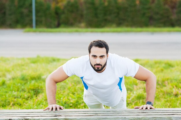 Portret sportieve man 30s in sportkleding doet push-ups in groen park.