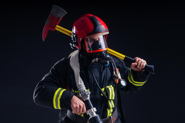 Portret sterke brandweerman in vuurvast uniform met een bijl in zijn handen zwarte achtergrond studio