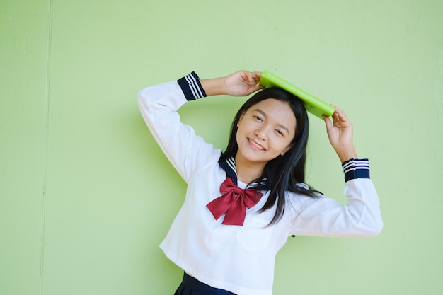 Portret student jong meisje in uniforme school met groen boek op groene achtergrond, Aziatisch meisje, tiener.