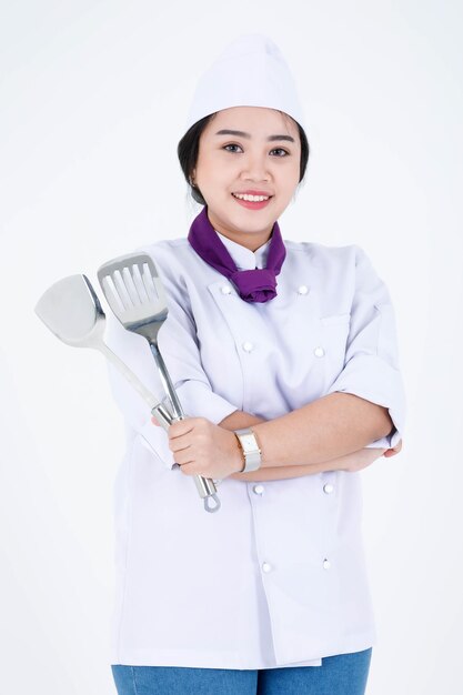 Portret studio shot van Aziatische professionele restaurant koken vrouwelijke chef-kok in uniform kok staande glimlachende blik op camera met spatel flipper turner gekruiste armen op witte achtergrond.