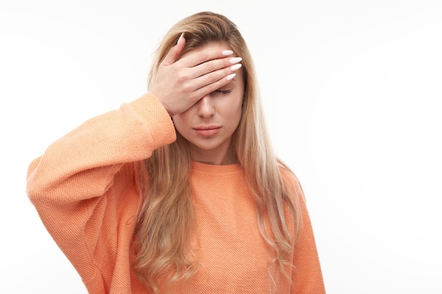 Portret trieste blonde jonge vrouw legde hand op voorhoofd geïsoleerd op witte studio achtergrond Fout gemaakt overstuur en depressiefxA