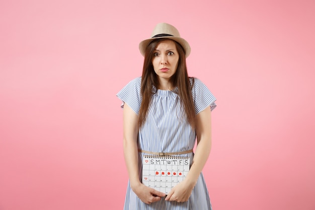 Portret trieste ziekte vrouw in blauwe jurk met perioden kalender voor het controleren van menstruatiedagen hand op buik geïsoleerd op roze achtergrond. medisch, gezondheidszorg, gynaecologisch concept. ruimte kopiëren