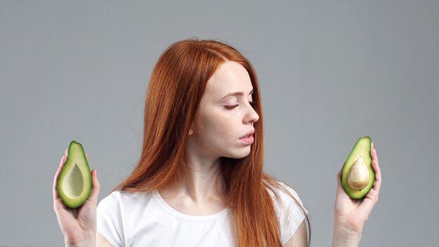 Portret van aantrekkelijk meisje glimlachen die gesneden avocado bekijken