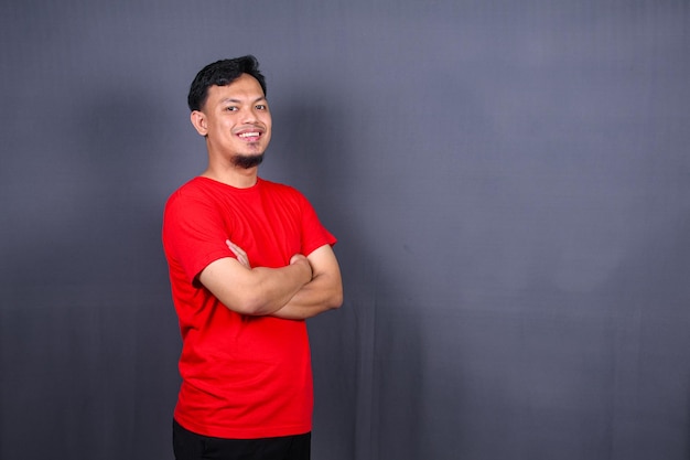 Portret van aantrekkelijke Aziatische man in rood t-shirt staande met gekruiste armen geïsoleerd grijze achtergrond