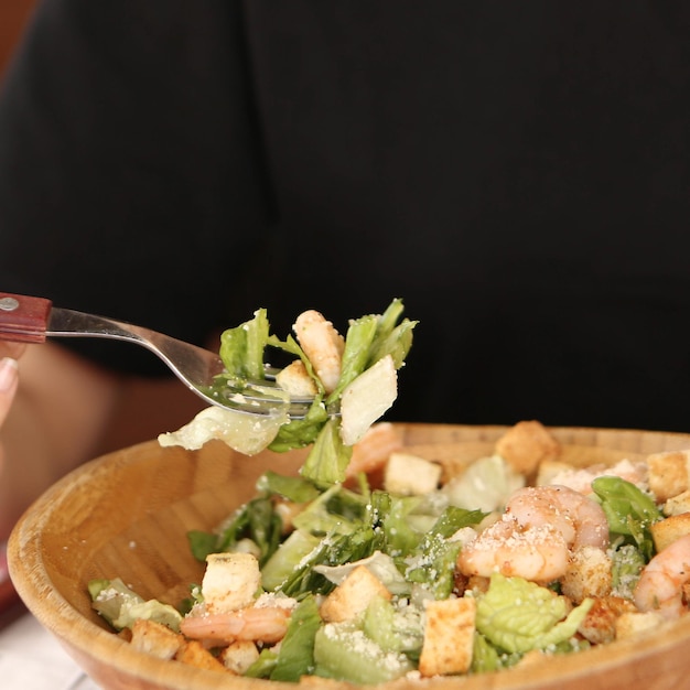 Portret van aantrekkelijke blanke lachende vrouw die salade eet, focus op hand en vork.