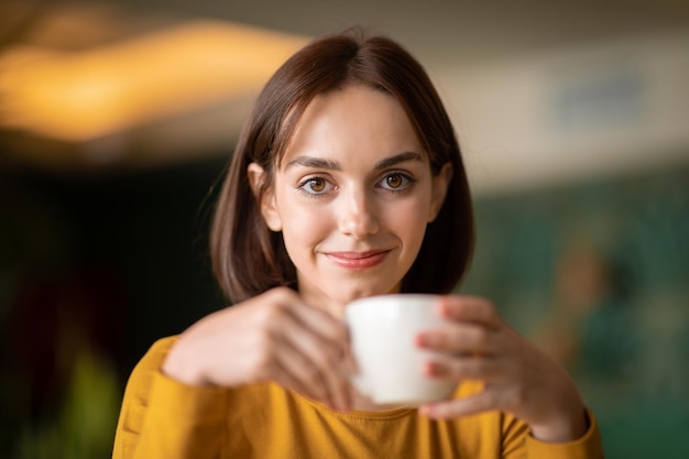 Portret van aantrekkelijke brunette jonge vrouw koffie drinken