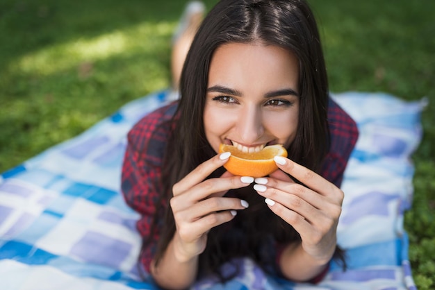 Portret van aantrekkelijke brunette vrouw liggend op groen gras in de buitenlucht eten oranje fruit kopieerruimte voor uw reclameboodschap of inhoud gelukkig vegetarische gezonde levensstijl